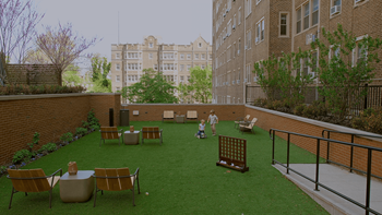 A man is standing in a courtyard with a green lawn and a brick wall.